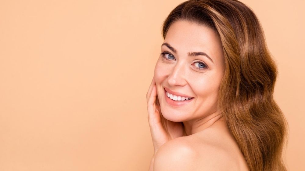 a women is smiling and touching her cheek | Feature | 5 Ultherapy Benefits For Looking Younger